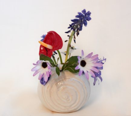 Bunte Blumenarrangements in einer hellen, spiralförmigen Vase.